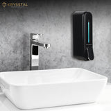 Black soap dispenser mounted on a gray wall above a white sink with tap.