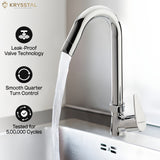 A chrome deck-mounted kitchen faucet with a curved high-arc spout running water into a stainless steel sink, highlighting its features: Leak-Proof Valve Technology, Smooth Quarter Turn Control, and Tested for 5,00,000 Cycles.