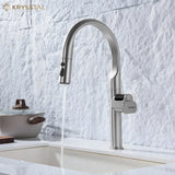 Modern kitchen faucet with water flowing into a sink against a textured white wall, featuring the Krysstal brand.