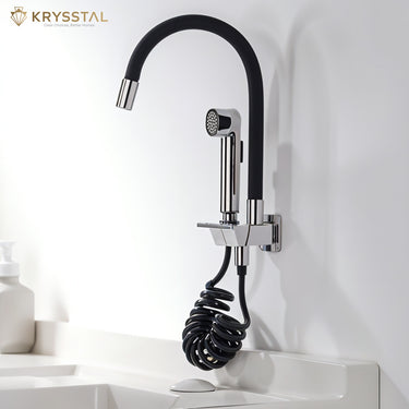 A black chrome finish flexible dual flow kitchen sink tap with hand shower mounted on a white wall