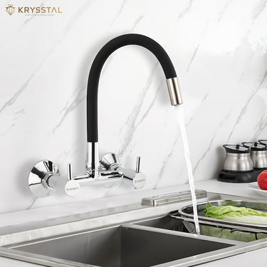 A wall-mounted kitchen sink mixer tap with a flexible silicone spout and chrome finish with flowing water fitted on a white textured wall.