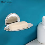 Silver soap dish reflecting on holder, carrying soap, mounted on blue wall with white shampoo bottle on right.