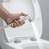 Hand holding a Krysstal ABS Health Faucet over a toilet with water flowing.