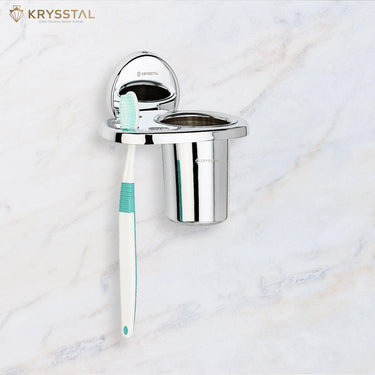 Silver stainless steel toothbrush holder on white tile with a blue and white toothbrush reflecting light.
