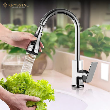 A silver-colored kitchen sink faucet aerator with handheld water spray technology is shown while washing the leaf, on a blurred background