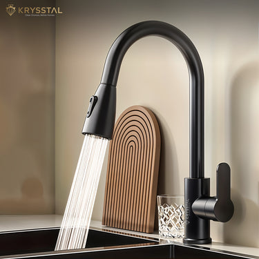 Black kitchen tap with round rotating spout and handle with pull out by hand features with flowing water on a sink fitted on a tile slab against a white background.