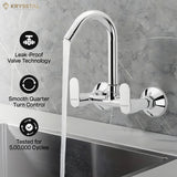 A silver kitchen sink mixer tap fitted on a grey wall with a flowing water into the sink & features like leak proof, smooth quarter & tested on the left side
