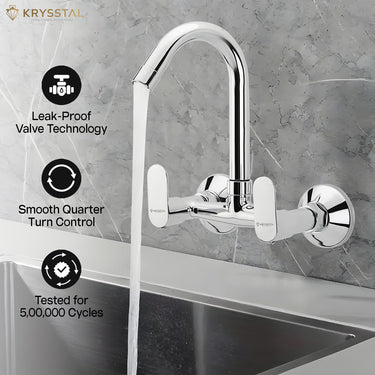 A silver kitchen sink mixer tap fitted on a grey wall with a flowing water into the sink & features like leak proof, smooth quarter & tested on the left side