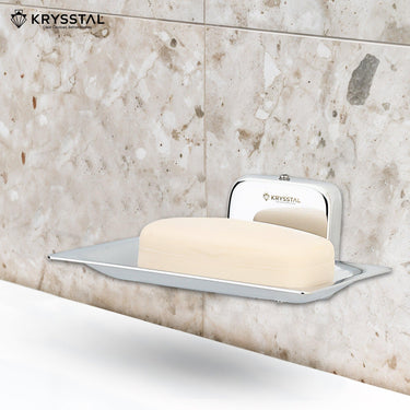 A square silver soap dish stand reflecting on the holder, carrying soap, mounted on a white textured wall with white washbasin at the bottom.