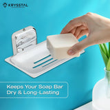 A silver square soap dish holder, carrying a hand-held soap, mounted on a blue wall with a written tagline at the bottom & beside a white pot with a plant.