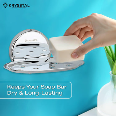 A silver soap dish holder, carrying a hand-held soap, mounted on a blue wall with a written tagline at the bottom & beside a white pot with a plant.