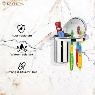 A silver toothbrush holder fixed on a white tile surface holding 3 colorful toothbrushes & 1 paste with its feature on the left side.