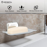 A wall-mounted square silver soap dish holding soap, reflecting on the holder, fitted on a brown textured wall, with its features on top & a white washbasin with tap at the bottom.