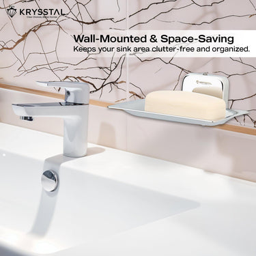 A space-saving silver square soap dish holding soap, reflecting on the holder, on a white textured wall, with white washbasin with silver tap at the bottom