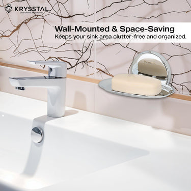 Wall-mounted & space saving silver soap dish holding soap, reflecting on the holder,on a white textured wall, with white washbasin with silver tap at the bottom