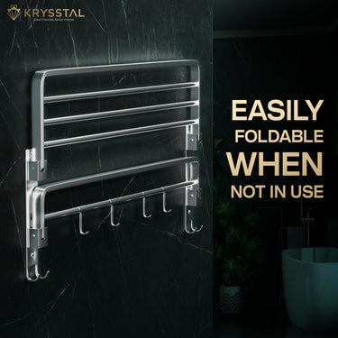 Foldable silver towel rack fixed on a black wall with tagged on right side "easily foldable when not in use