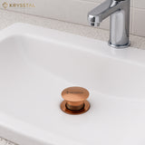 Rose gold sink drain stopper on a white sink with a silver faucet in the bathroom area.