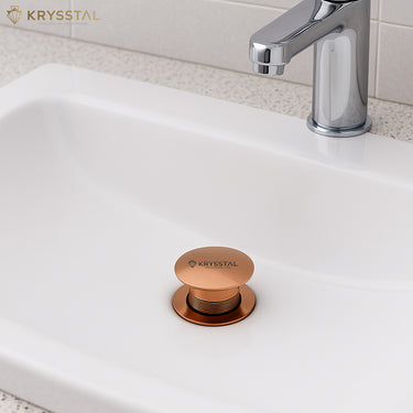 Rose gold sink drain stopper on a white sink with a silver faucet in the bathroom area.