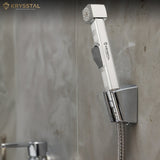 Silver health faucet sprayer gun mounted on wall hook against grey tiled background.